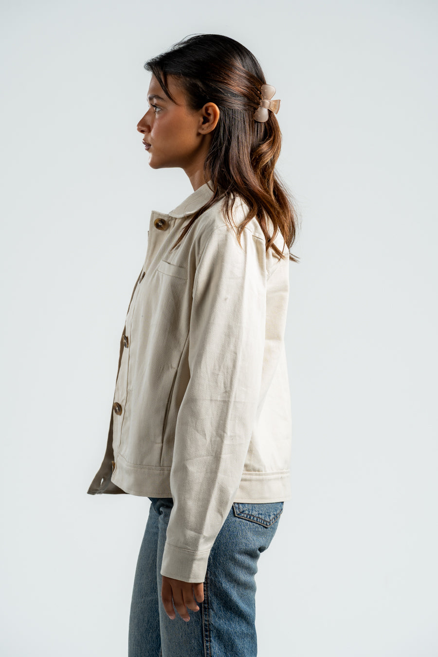 Woman wearing a beige jacket and blue jeans against a white background