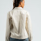 Person wearing a beige jacket and blue jeans on a plain background