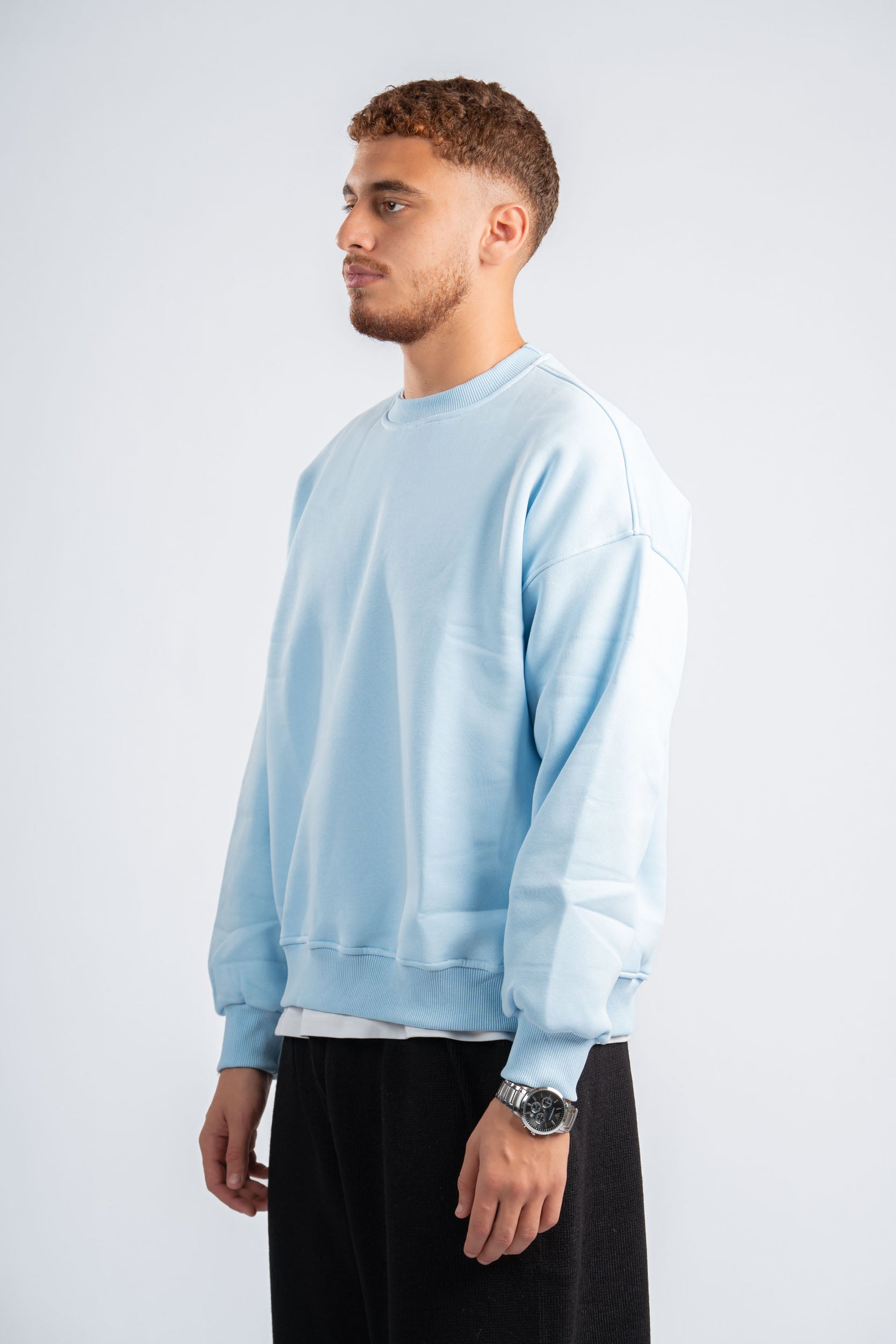 Man wearing a light blue sweatshirt and black pants on a white background
