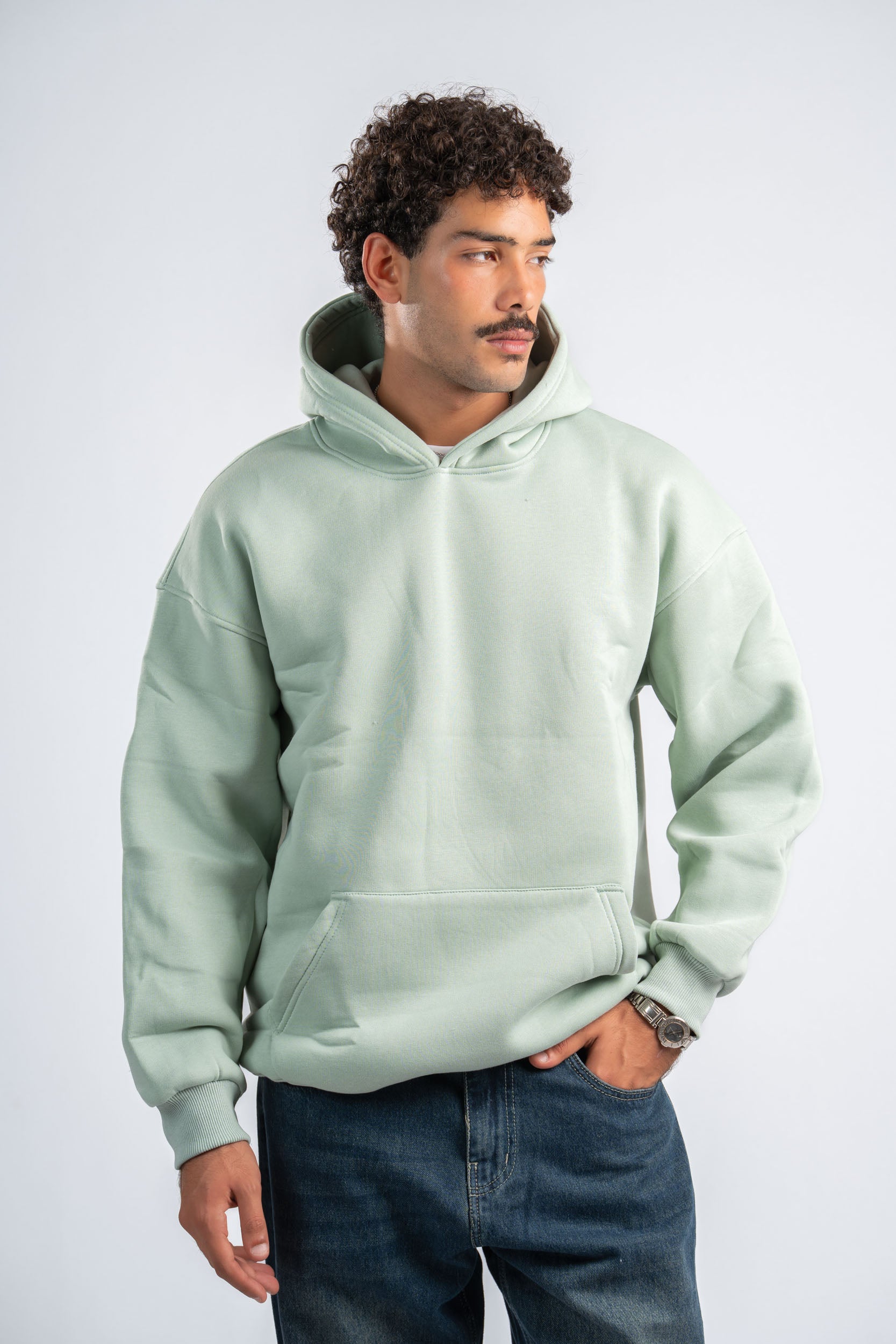 Man wearing a light green hoodie and blue jeans on a white background