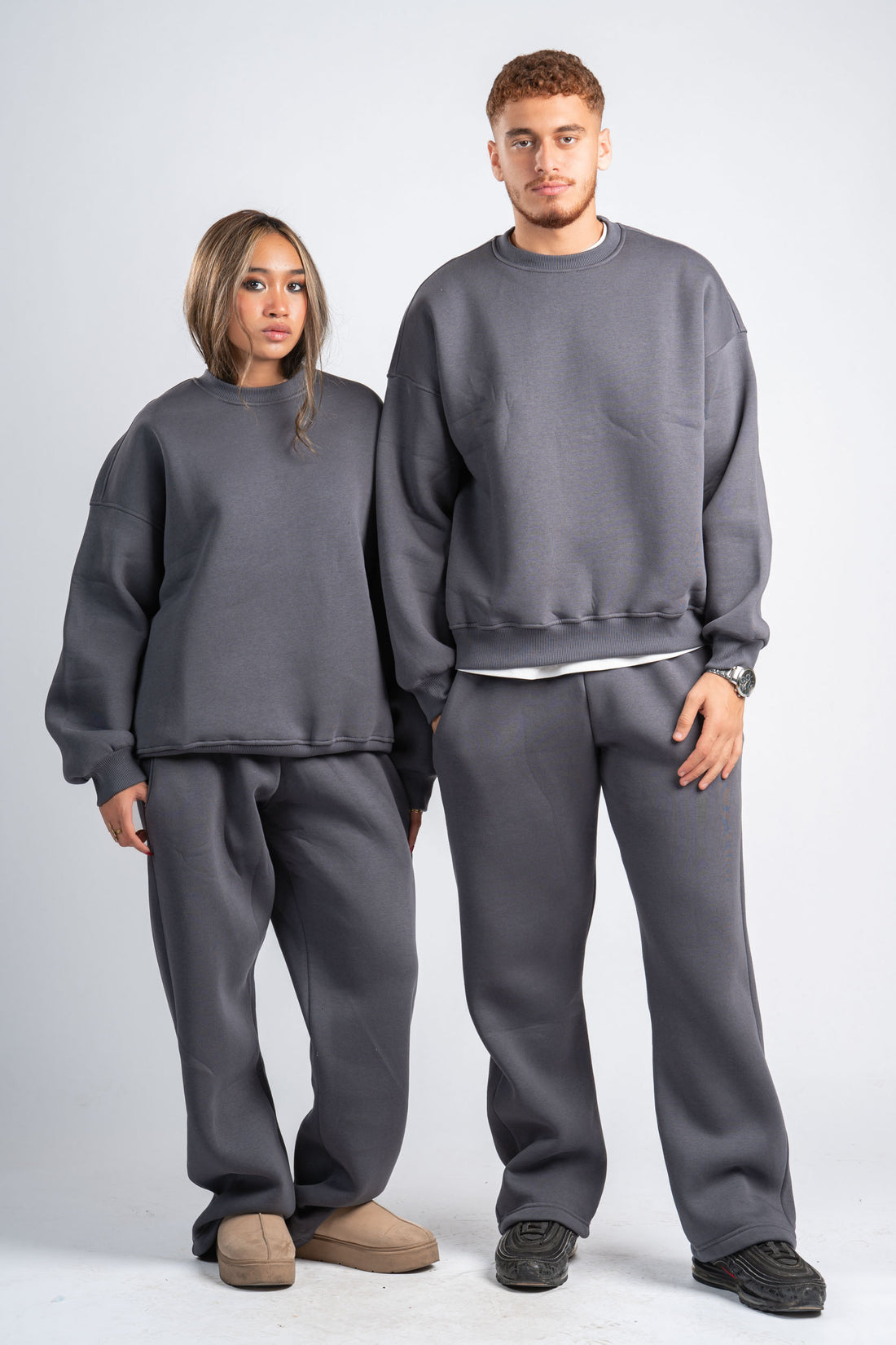 Two people wearing matching gray sweatshirt and pants sets on a plain background