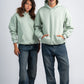 Two people wearing light green hoodies and dark jeans on a white background