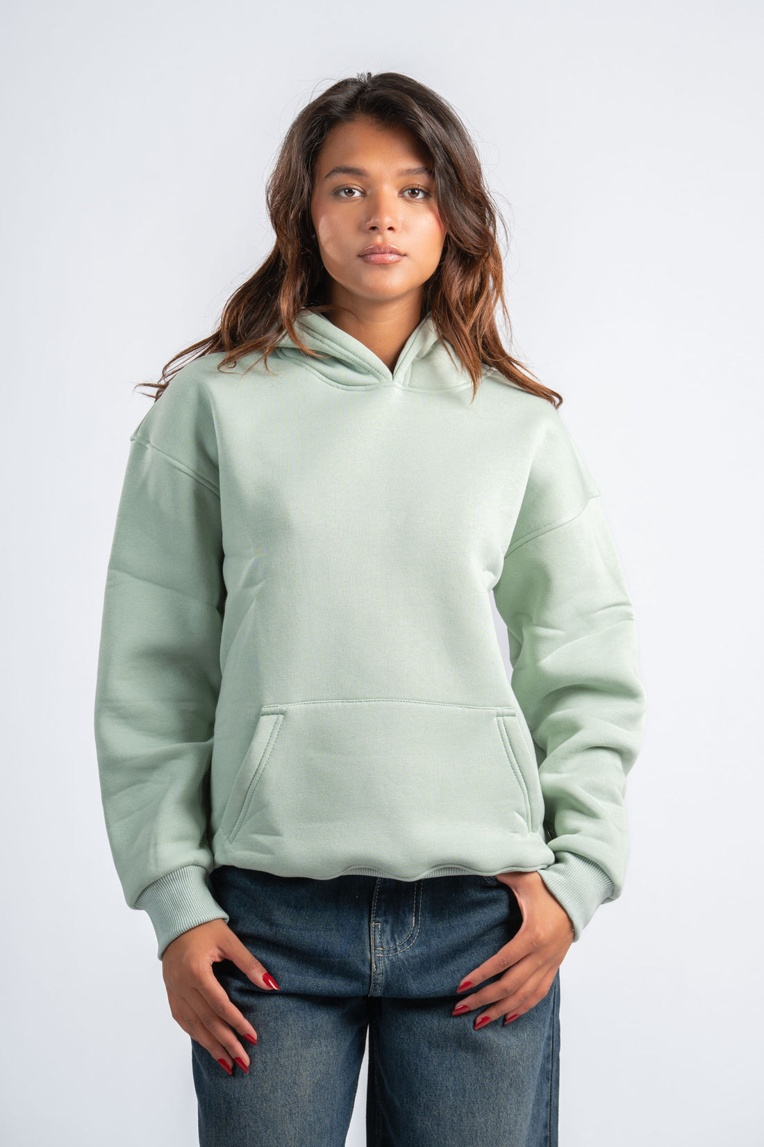Two people wearing light green hoodies and dark jeans on a white background