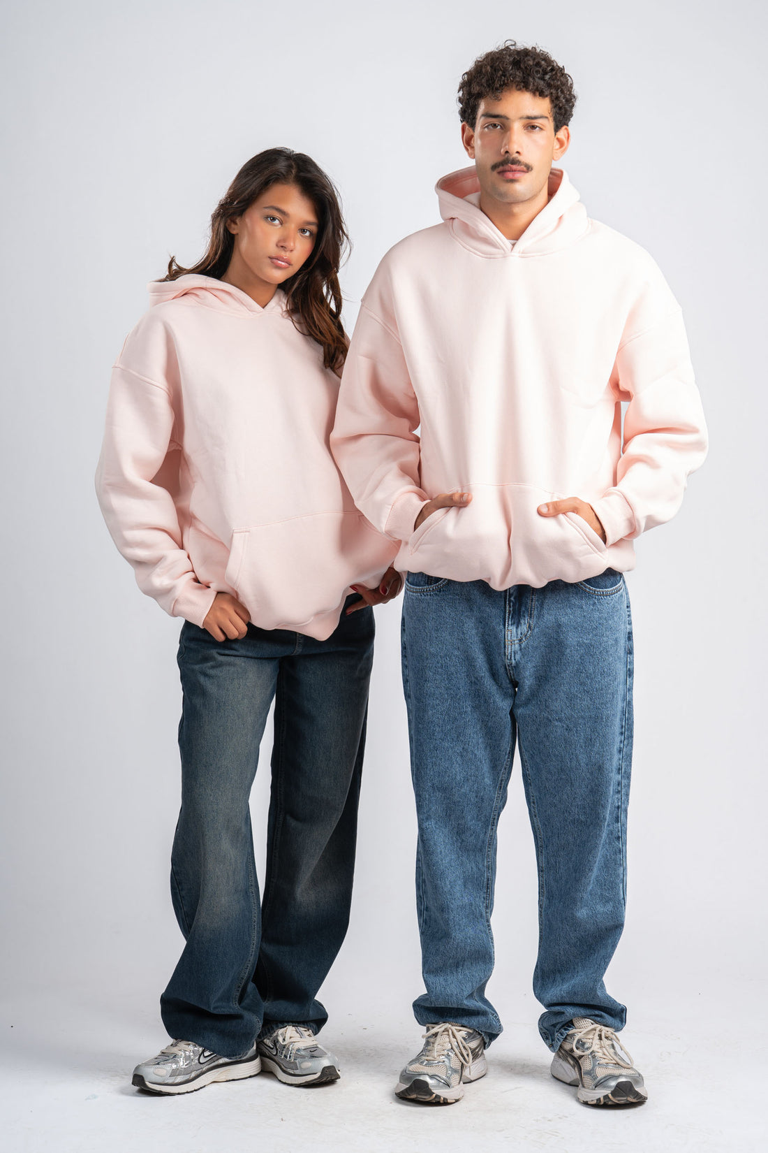 Two people wearing pink hoodies and blue jeans on a white background