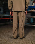Person wearing a beige jacket and pants standing in an industrial setting