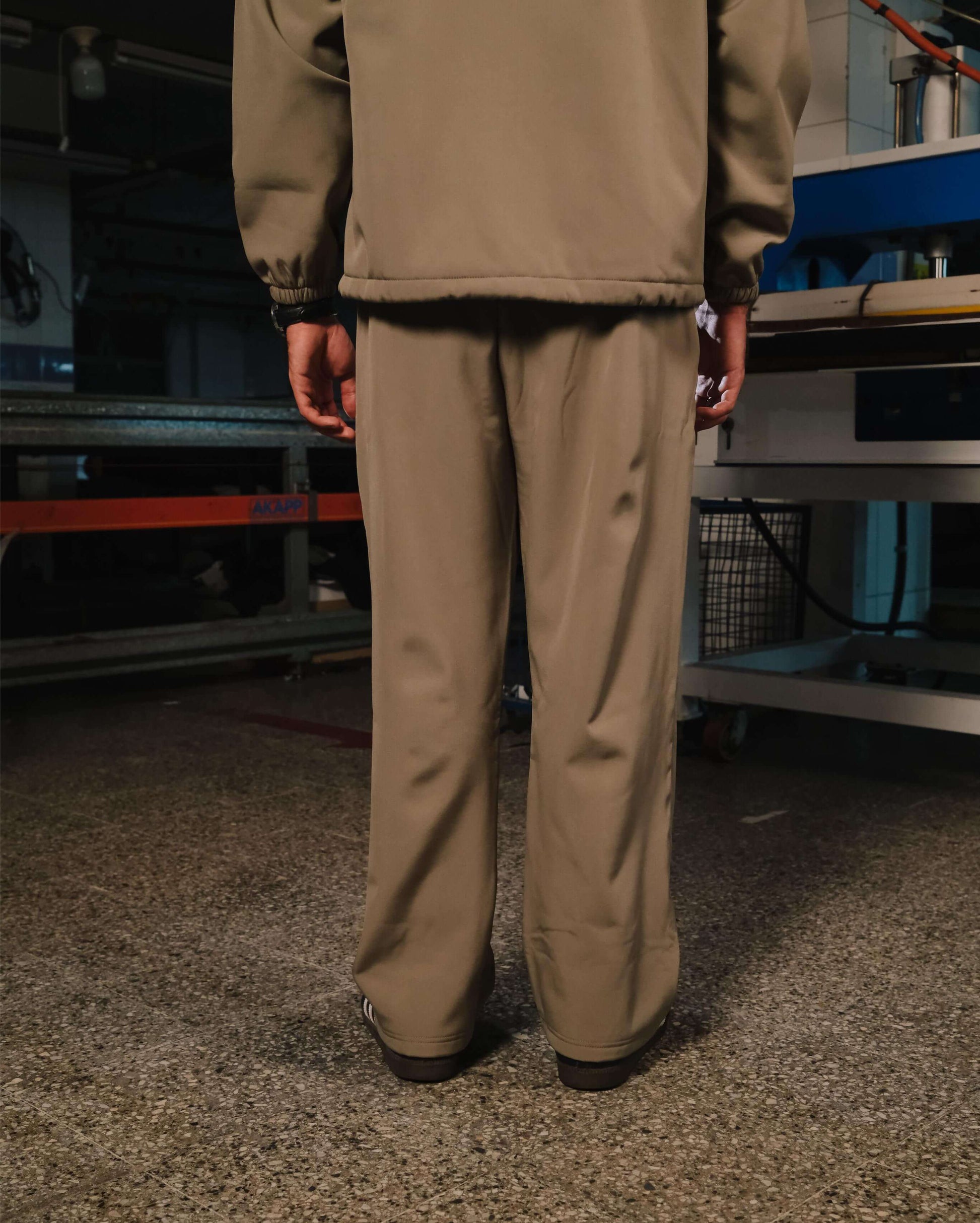 Person wearing a beige jacket and pants standing in an industrial setting