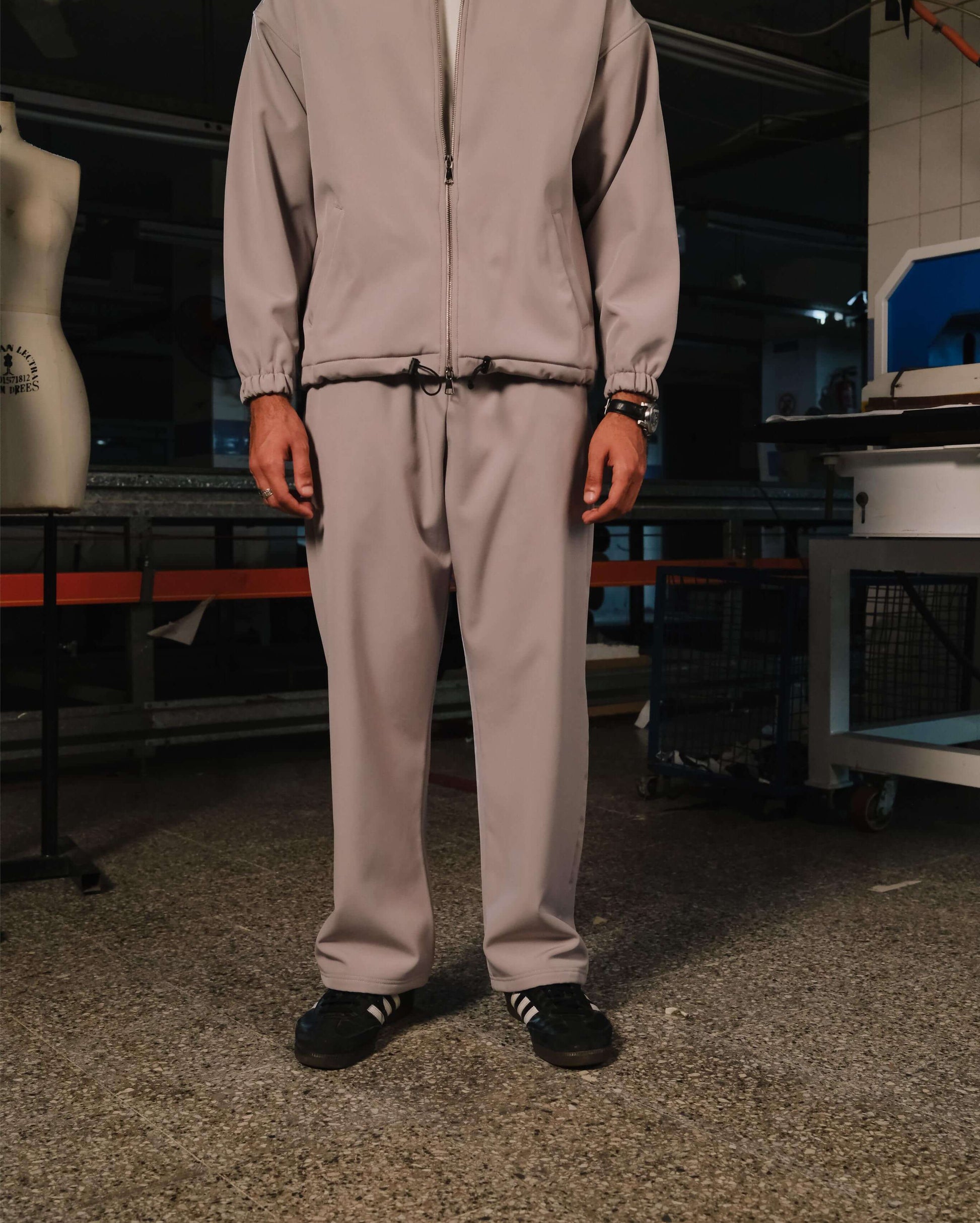 Person wearing a beige tracksuit in an indoor setting with mannequin and equipment.