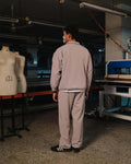 Person in a gray outfit standing in a workshop with mannequins and equipment.