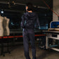 Person in a dark outfit standing in a workshop with mannequins and equipment.