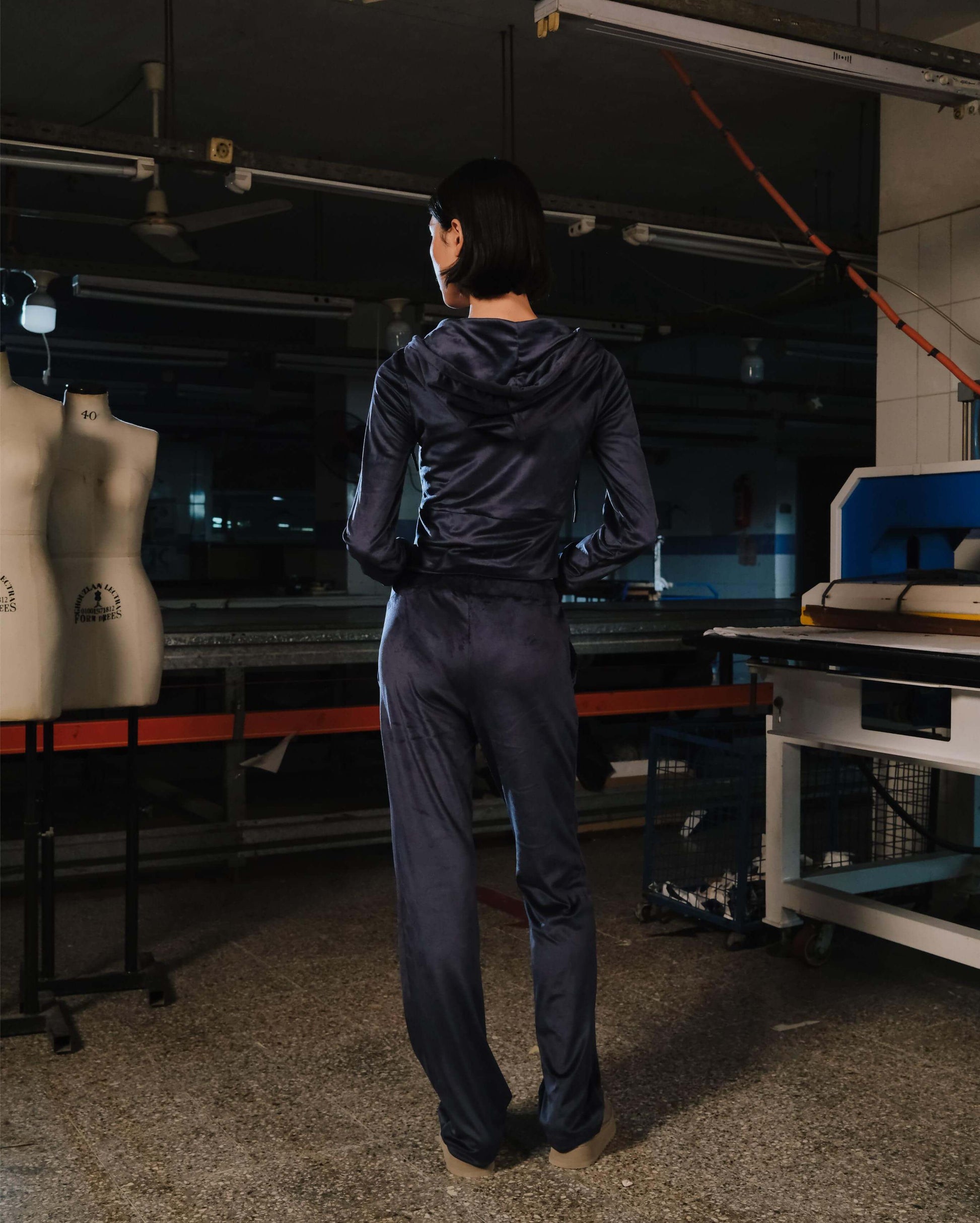Person in a dark outfit standing in a workshop with mannequins and equipment.