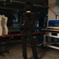 Person wearing a black outfit in a workshop setting with sewing machines and mannequins.