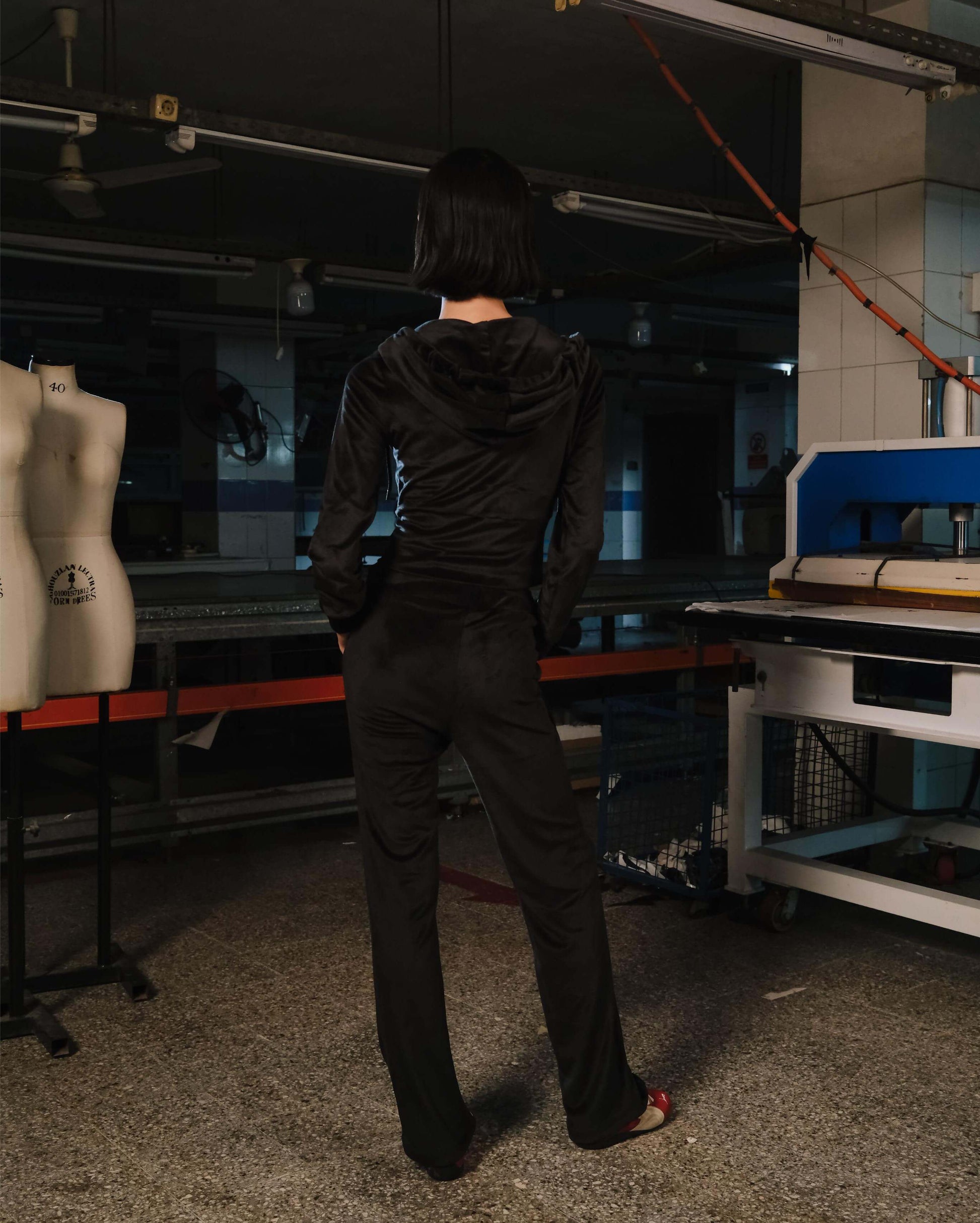 Person wearing a black outfit in a workshop setting with sewing machines and mannequins.