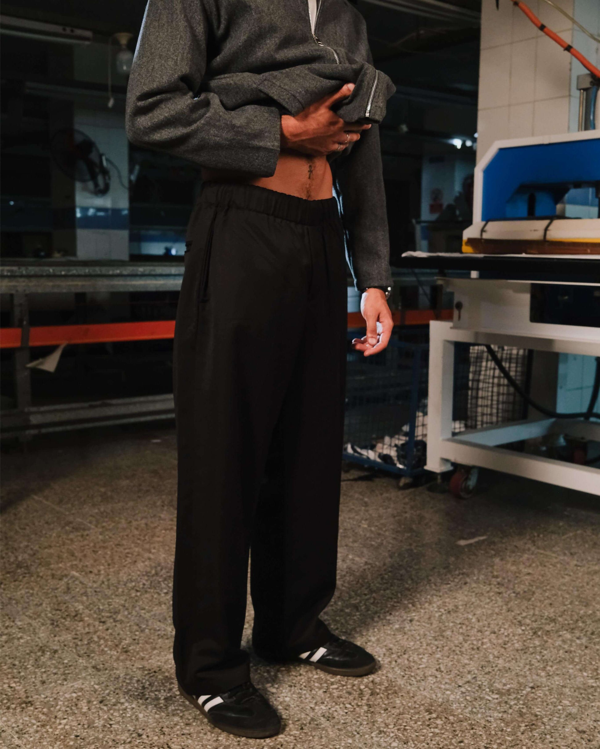 Person wearing a gray sweatshirt and black pants standing in an industrial setting.