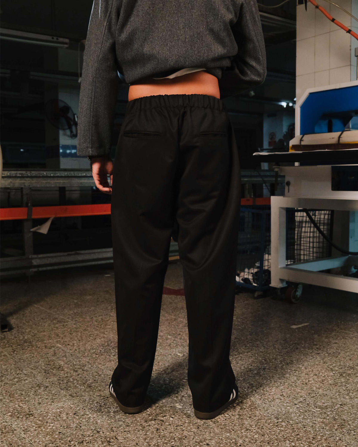 Person wearing black pants and a gray sweatshirt in an industrial setting