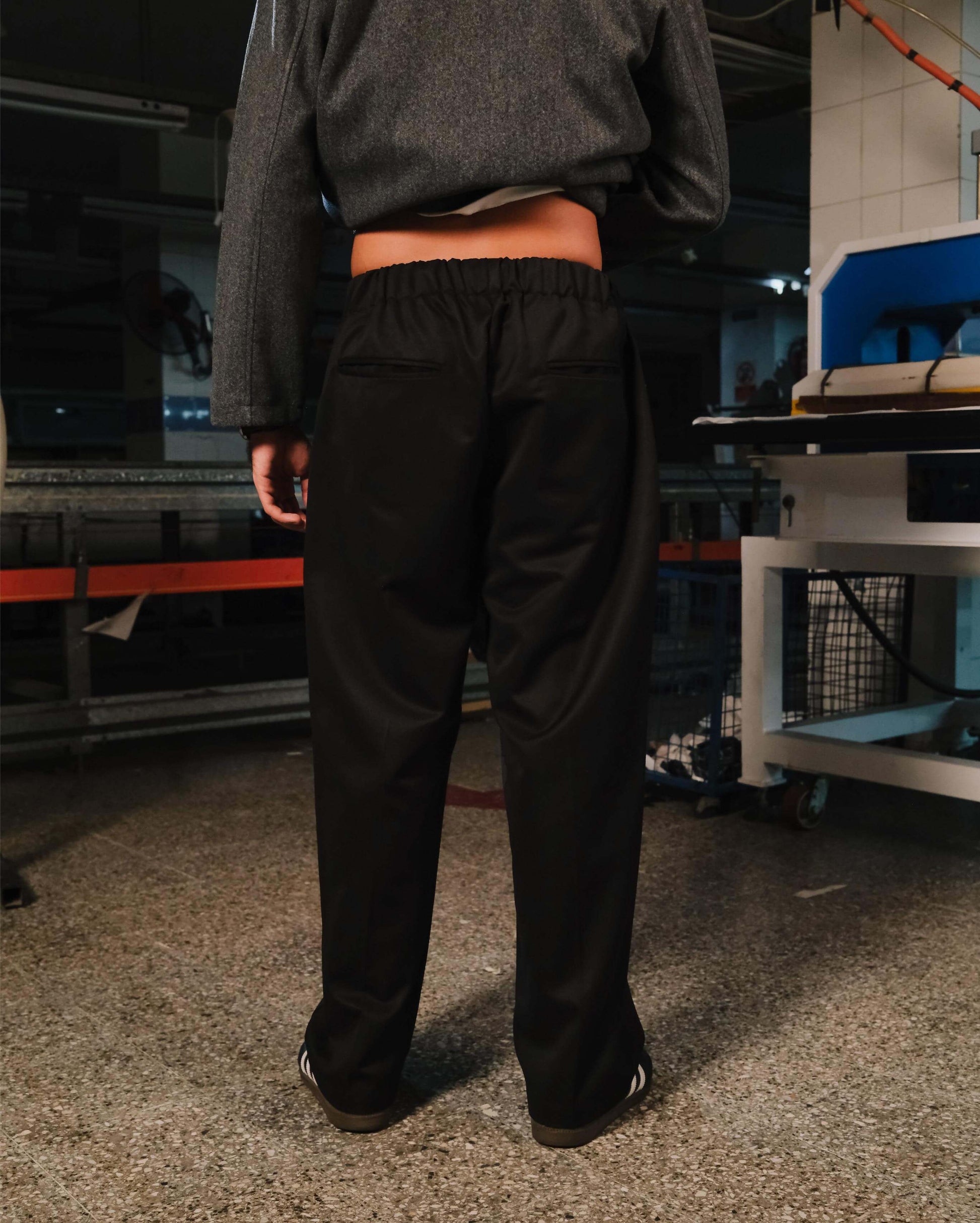 Person wearing black pants and a gray sweatshirt in an industrial setting