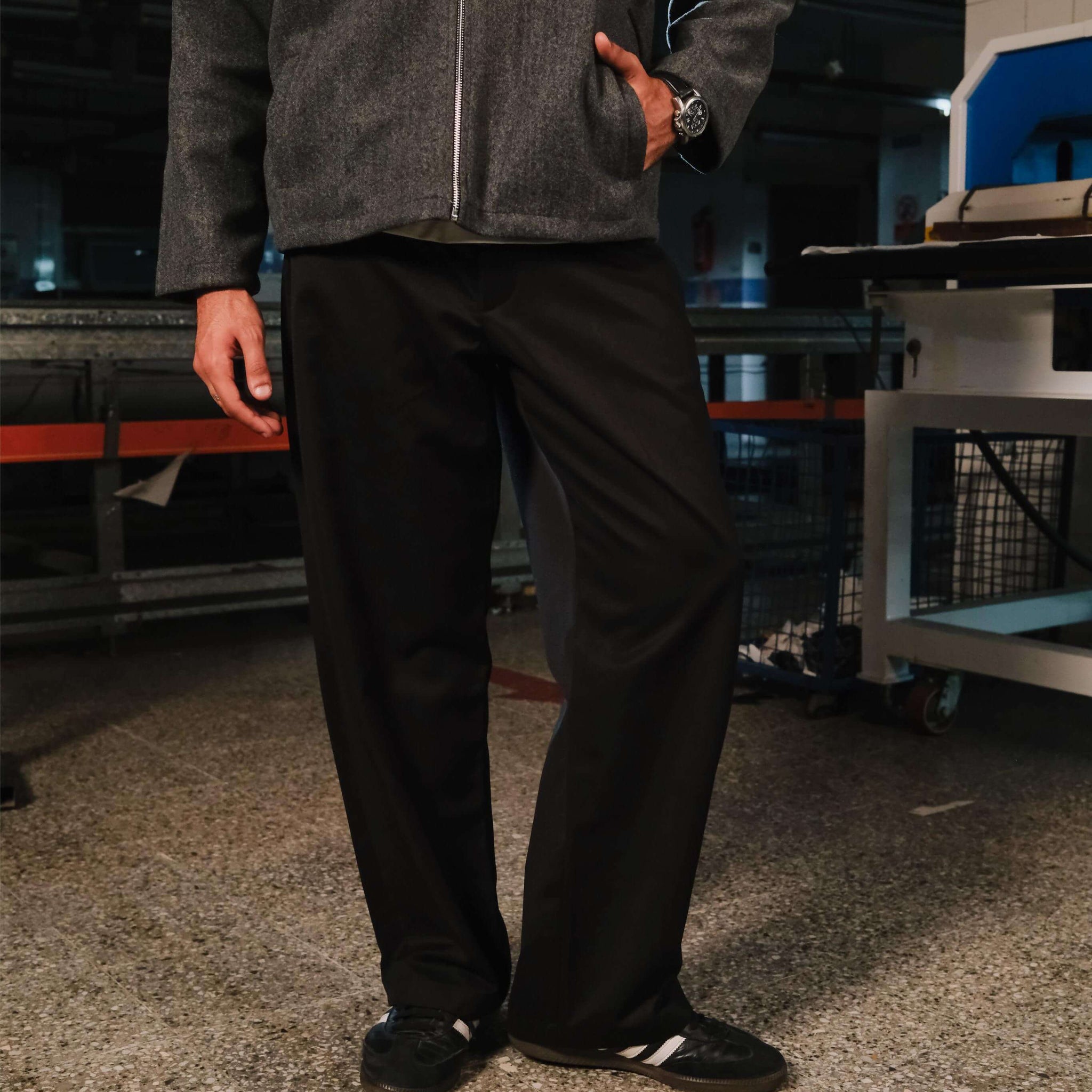 Person wearing a gray jacket and black pants standing in an industrial setting.