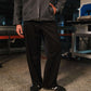 Person wearing a gray jacket and black pants standing in an industrial setting.