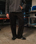 Person wearing a gray jacket and black pants standing in an industrial setting.