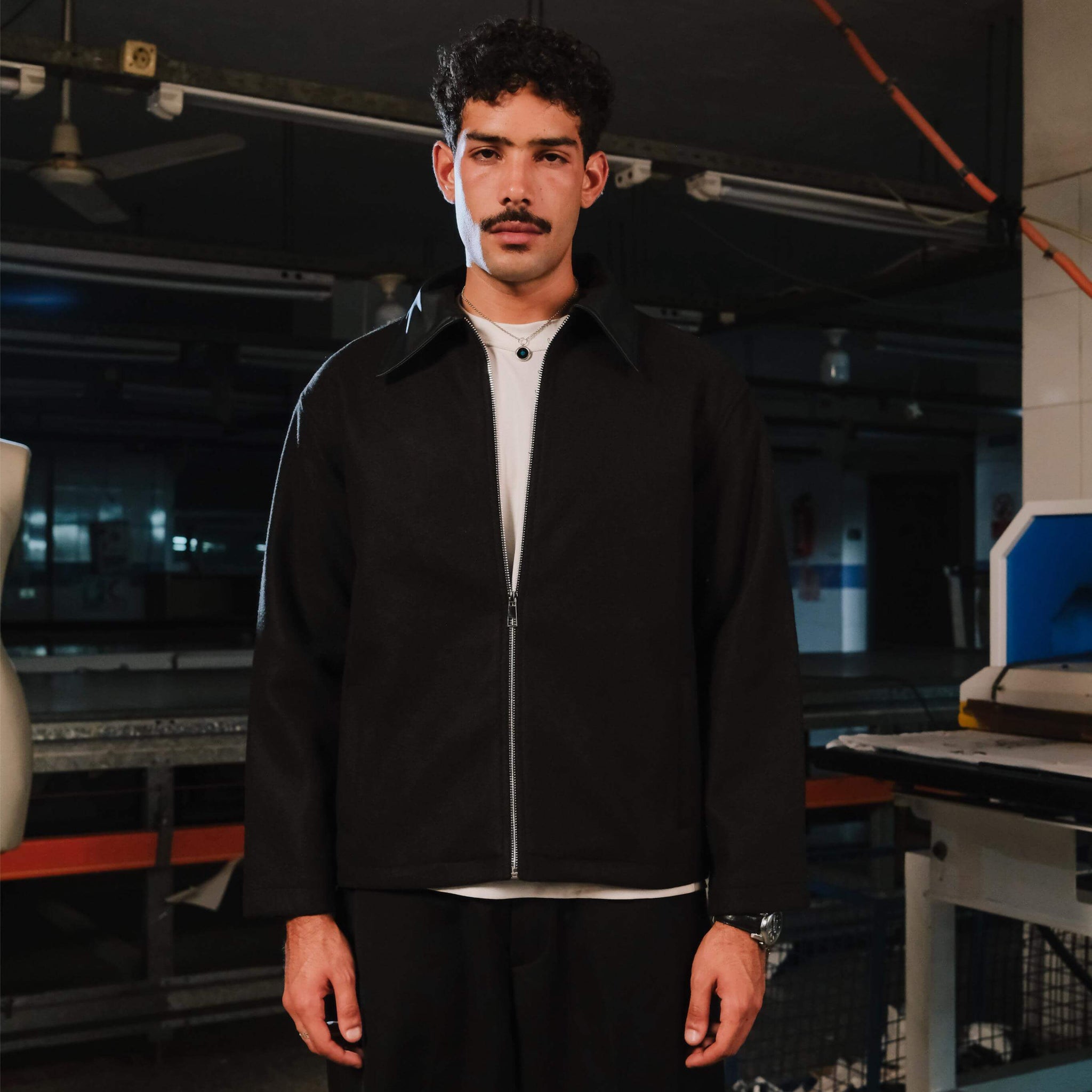 Man wearing a black jacket and white shirt in an industrial setting