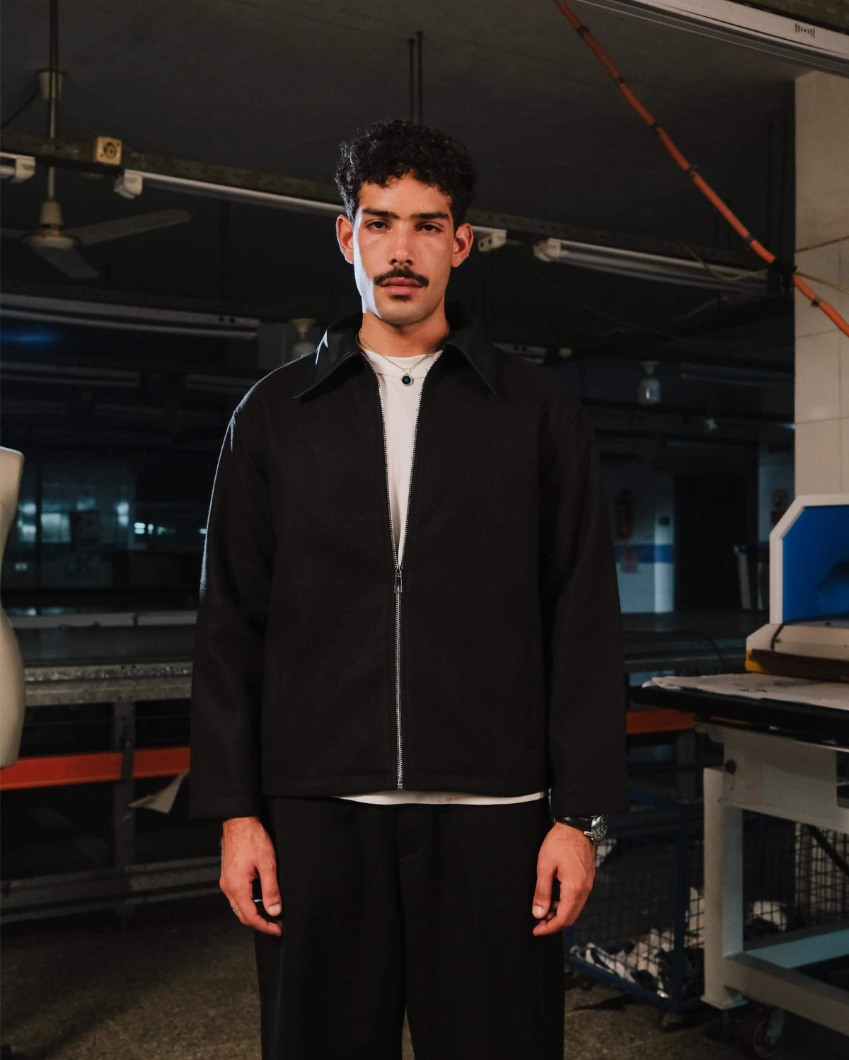 Man wearing a black jacket and white shirt in an industrial setting