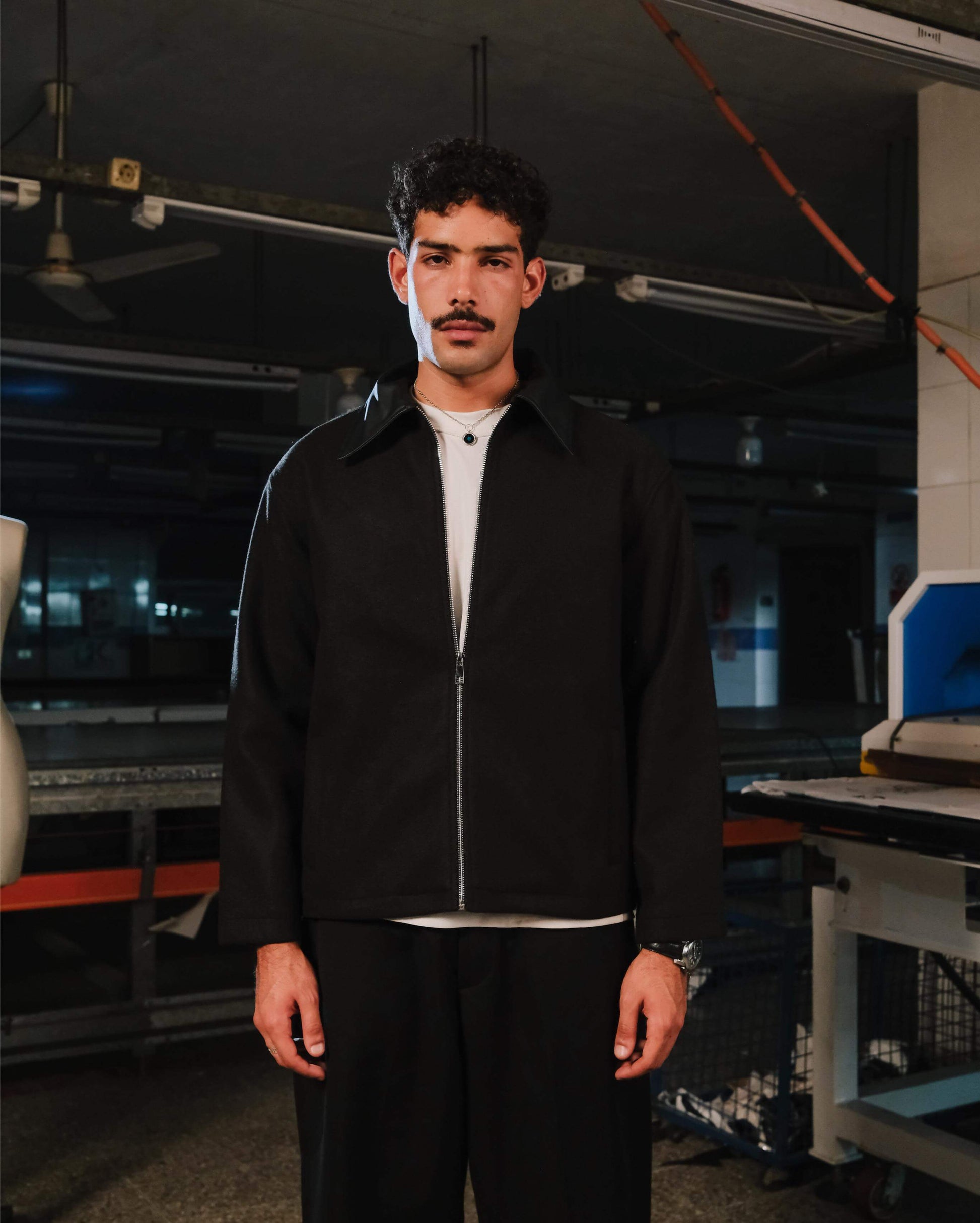 Man wearing a black jacket and white shirt in an industrial setting