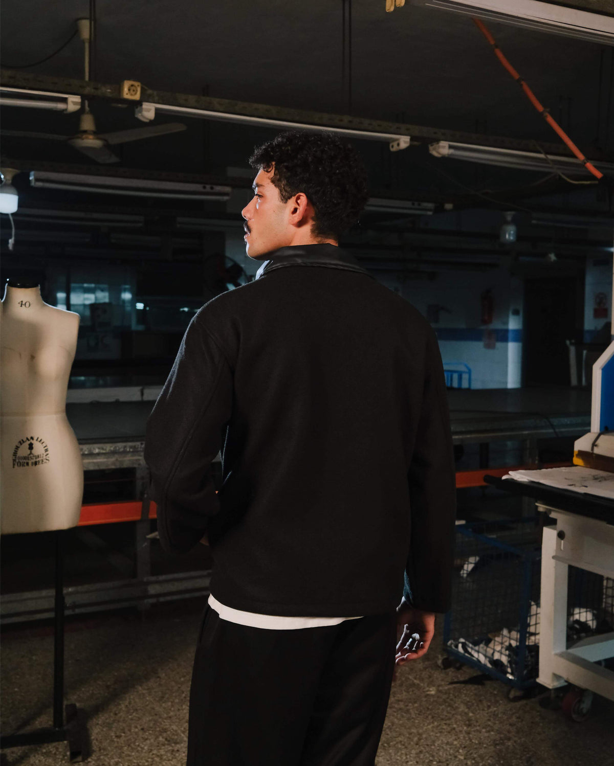 Person wearing a black jacket in an indoor setting with equipment and a mannequin.