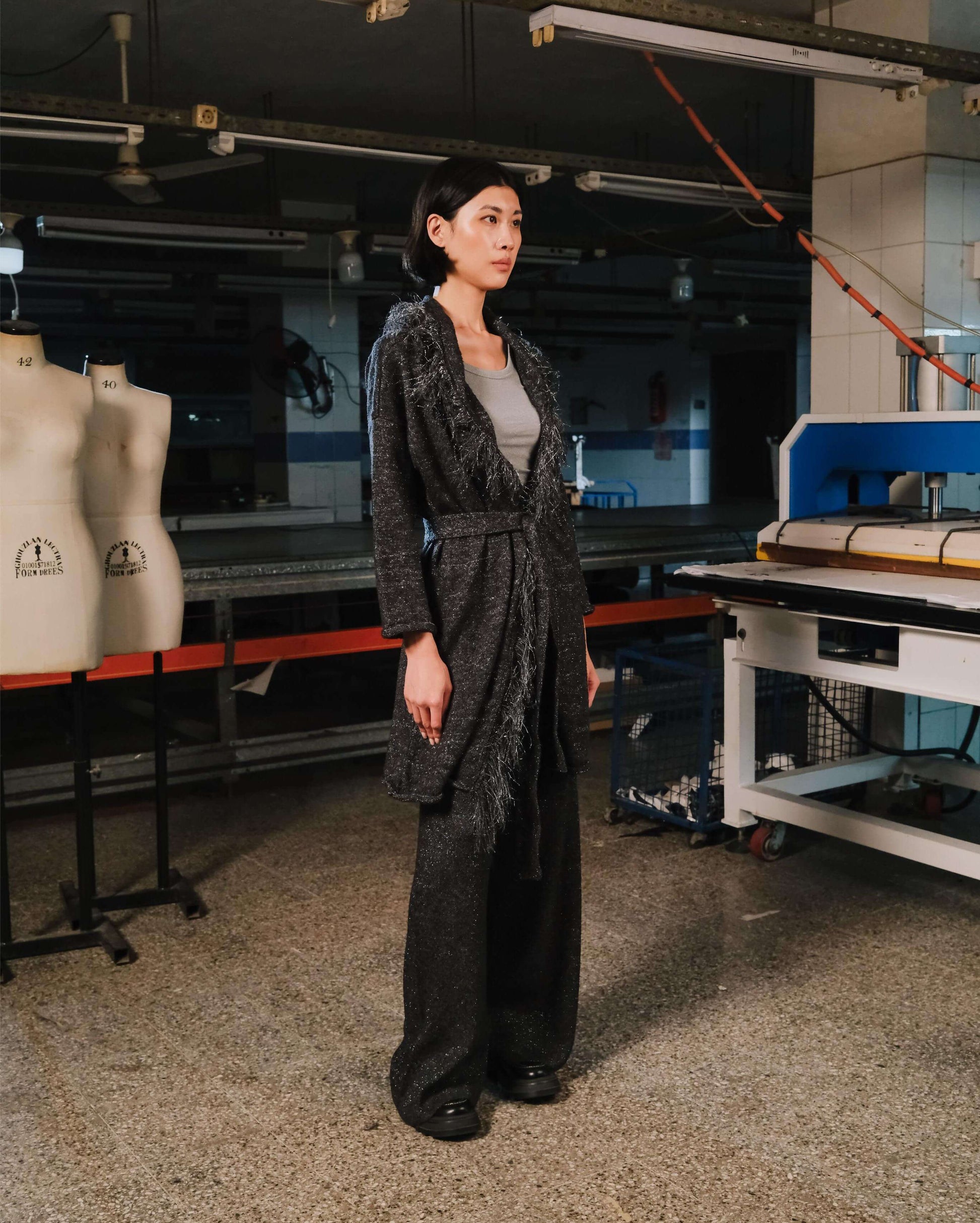 Person standing in a workshop or studio with sewing equipment and mannequins.