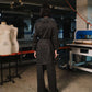 Person wearing a dark coat standing in a room with mannequins and equipment.