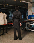 Person wearing a dark coat standing in a room with mannequins and equipment.