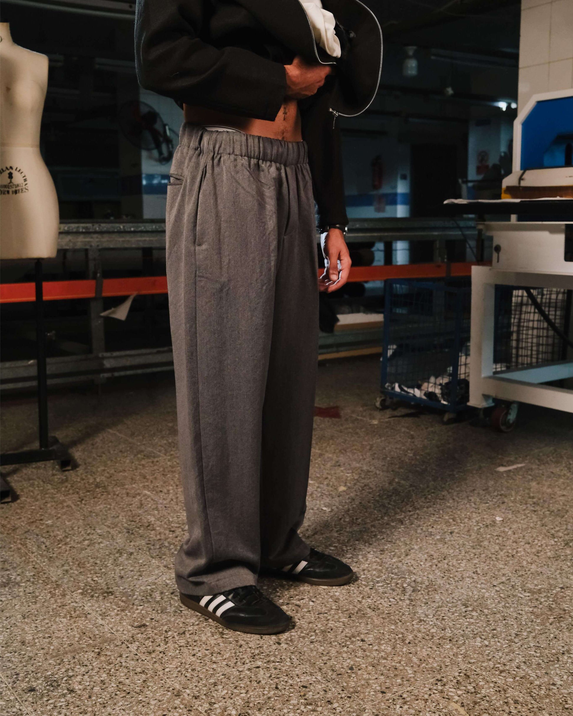 Person wearing gray pants and black shoes in an indoor setting with a mannequin and equipment in the background.