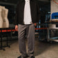 Man wearing a black jacket, white shirt, and gray pants standing in an indoor setting with equipment and mannequins in the background.