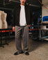 Man wearing a black jacket, white shirt, and gray pants standing in an indoor setting with equipment and mannequins in the background.