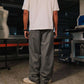 Person wearing a white t-shirt and gray striped pants in an indoor setting with machinery and equipment.