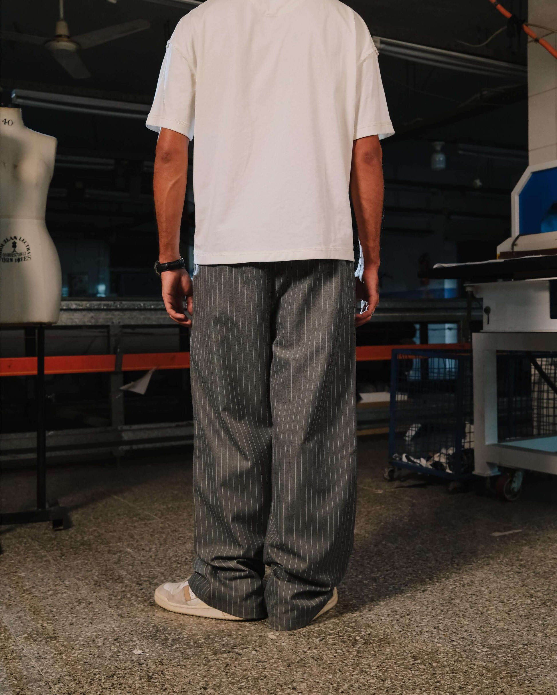 Person wearing a white t-shirt and gray striped pants in an indoor setting with machinery and equipment.