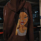 Brown hoodie with a face design on the back, worn by a person indoors.
