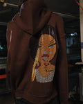 Brown hoodie with a face design on the back, worn by a person indoors.
