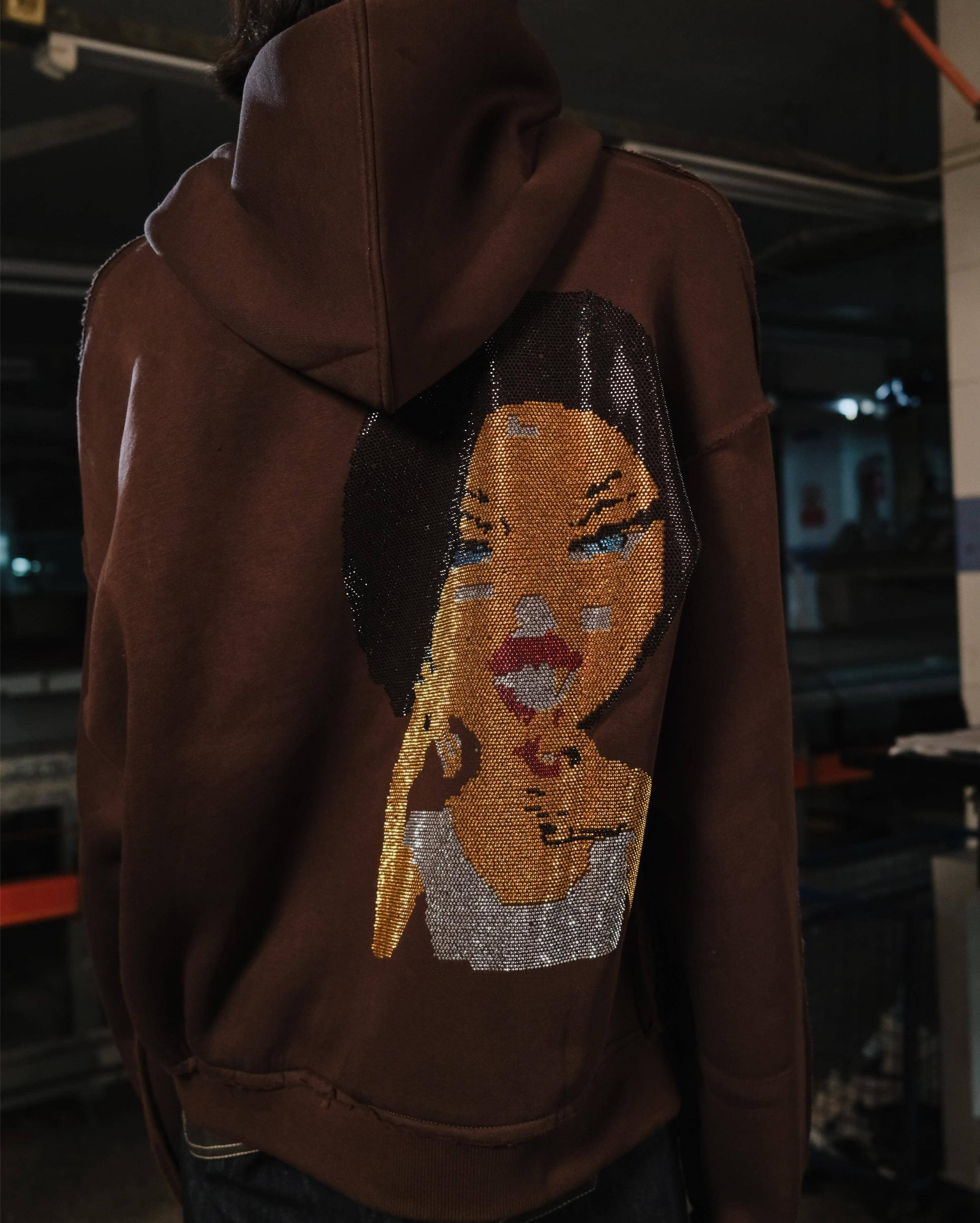 Brown hoodie with a face design on the back, worn by a person indoors.