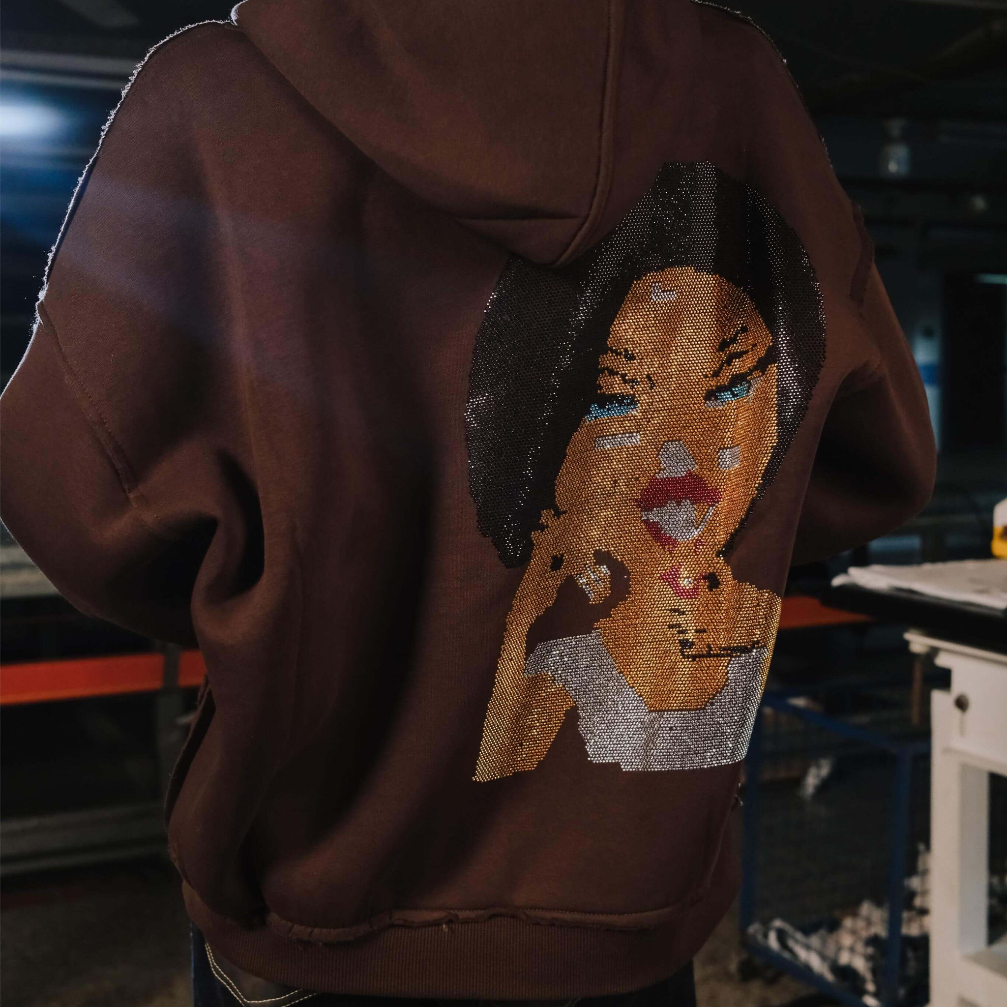 Brown hoodie with a face design on the back worn by a person indoors.
