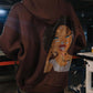 Brown hoodie with a face design on the back worn by a person indoors.