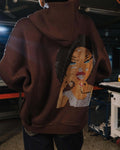 Brown hoodie with a face design on the back worn by a person indoors.