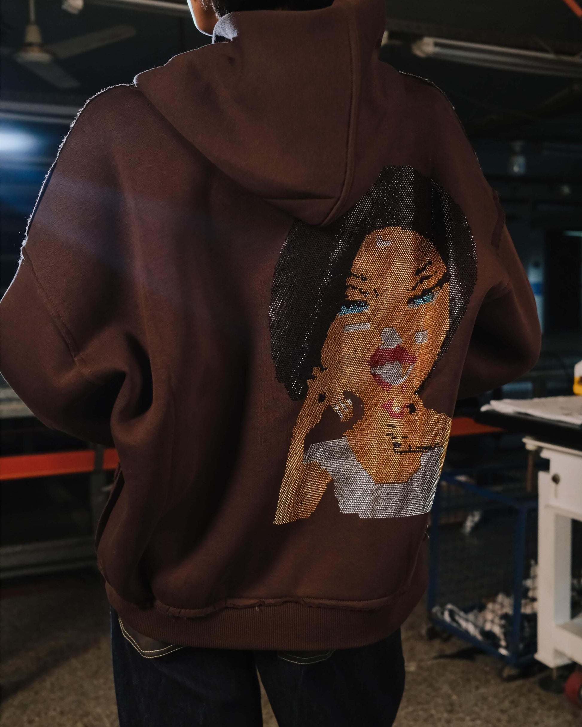 Brown hoodie with a face design on the back worn by a person indoors.