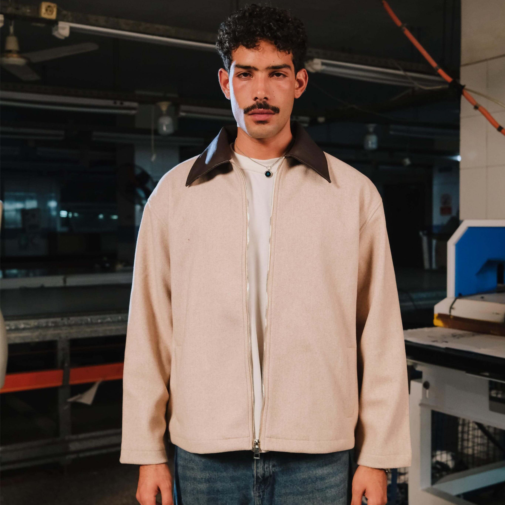 Man wearing a beige jacket with a dark collar in an industrial setting