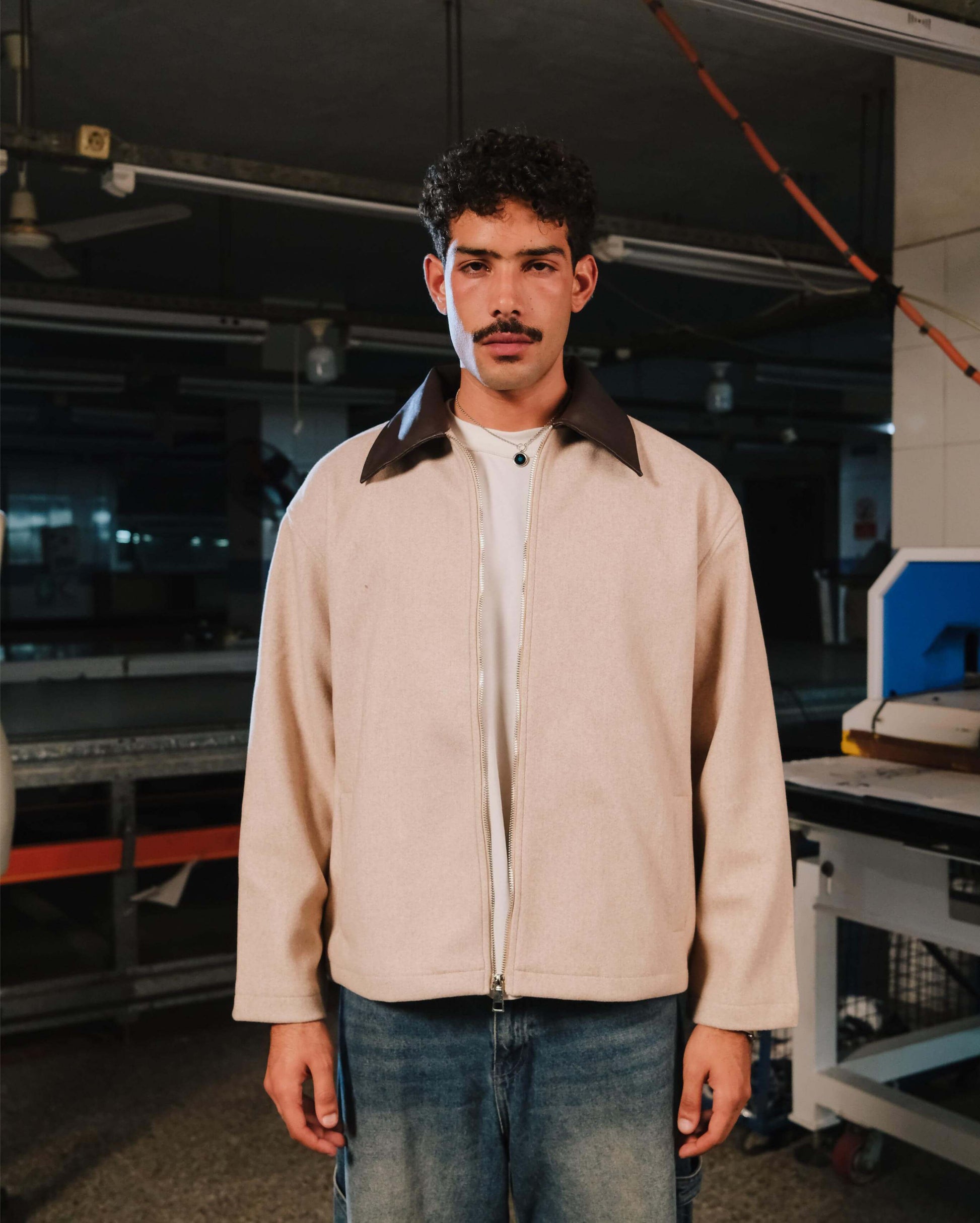 Man wearing a beige jacket with a dark collar in an industrial setting