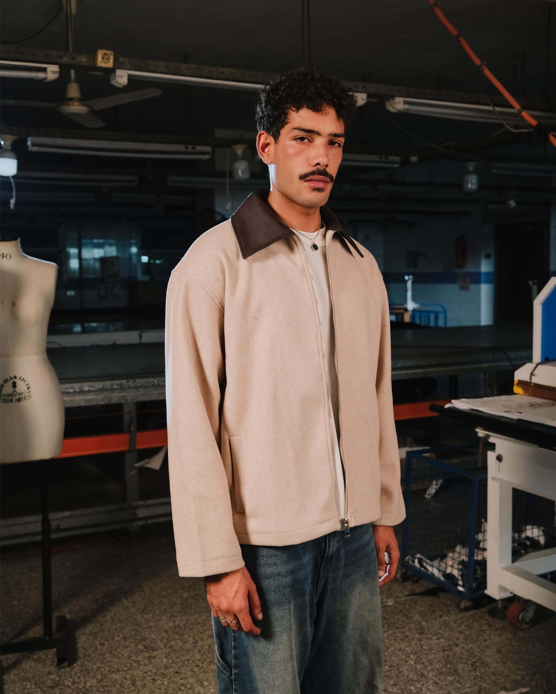 Man wearing a beige jacket with a brown collar in an industrial setting