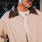 Man wearing a beige jacket with a brown collar, indoors.