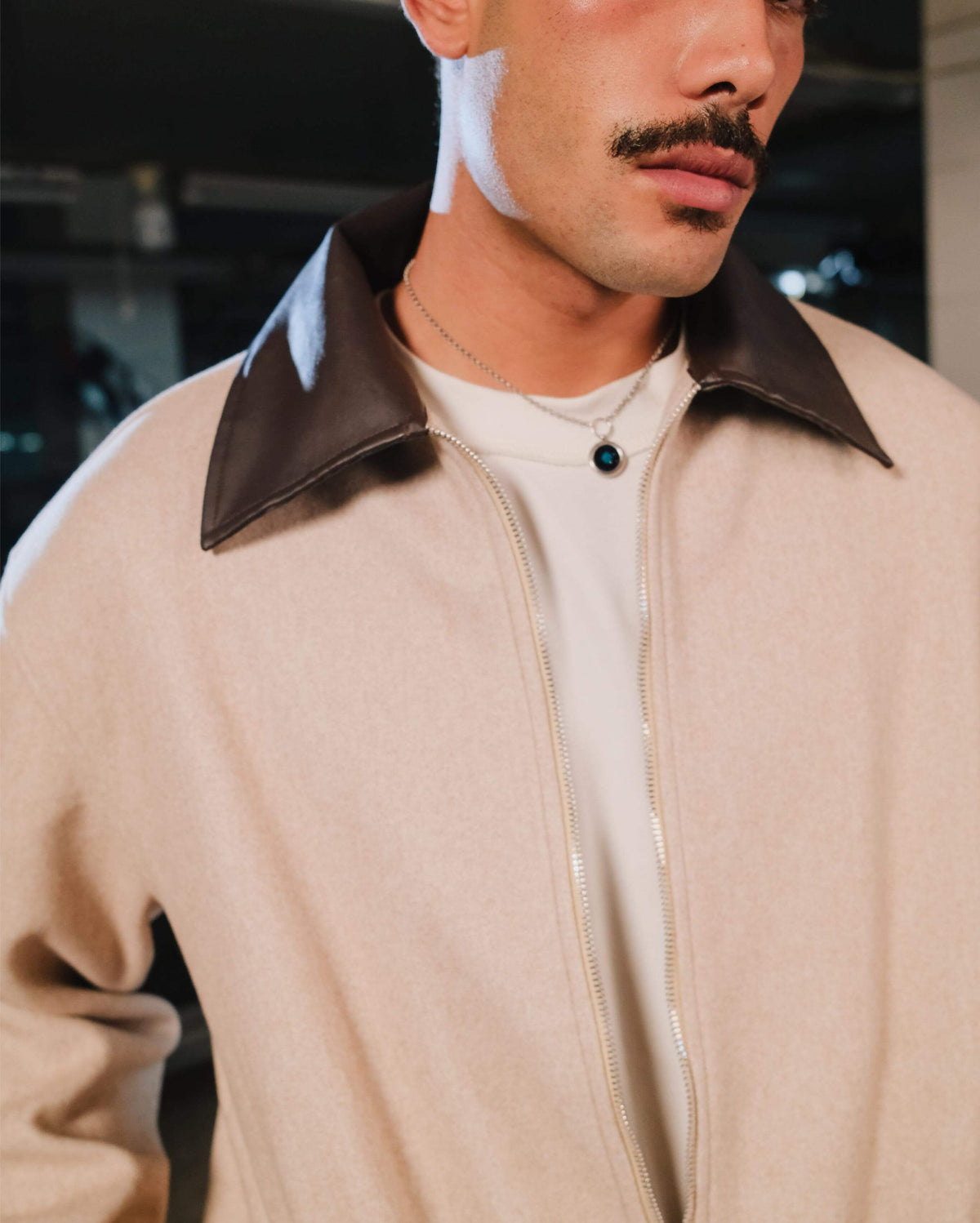 Man wearing a beige jacket with a brown collar, indoors.