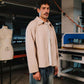Man wearing a beige jacket in a workshop setting with sewing machines and mannequins.