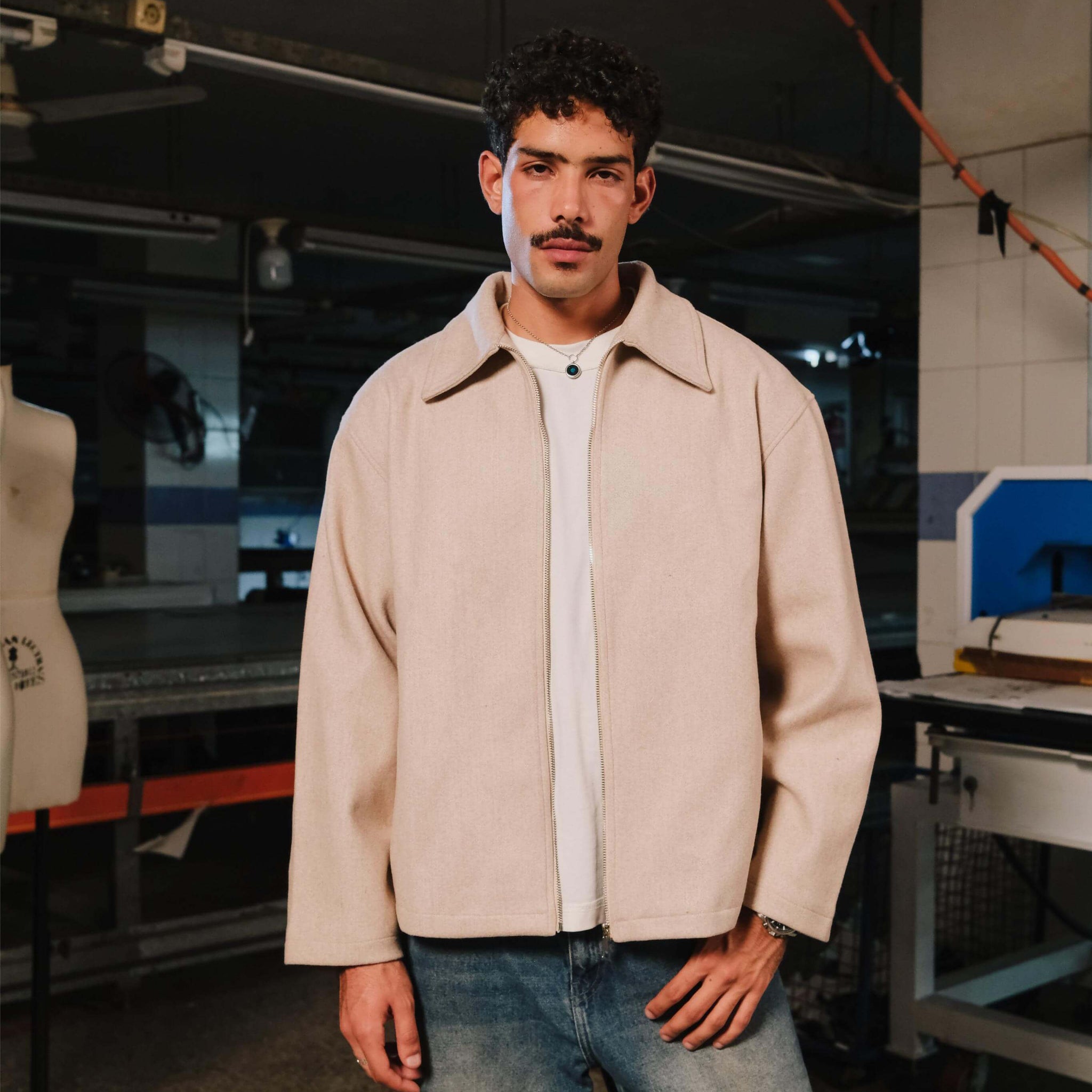 Man wearing a beige jacket and white shirt in a workshop setting