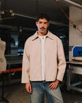 Man wearing a beige jacket and white shirt in a workshop setting