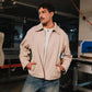 Man wearing a beige jacket and blue jeans standing in an industrial setting.